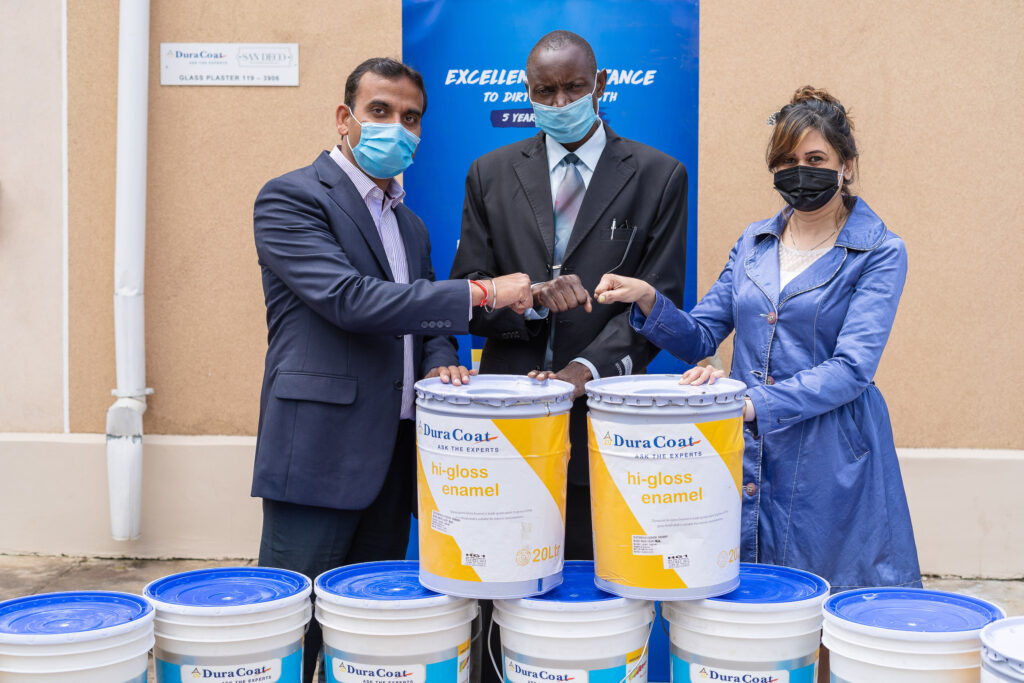 Corporate handover ceremony with representatives standing behind stacked donation buckets