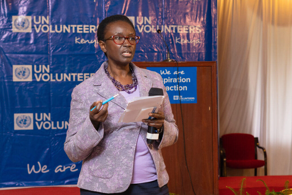 Speaker addressing guests in front of a UN Volunteers Kenya backdrop