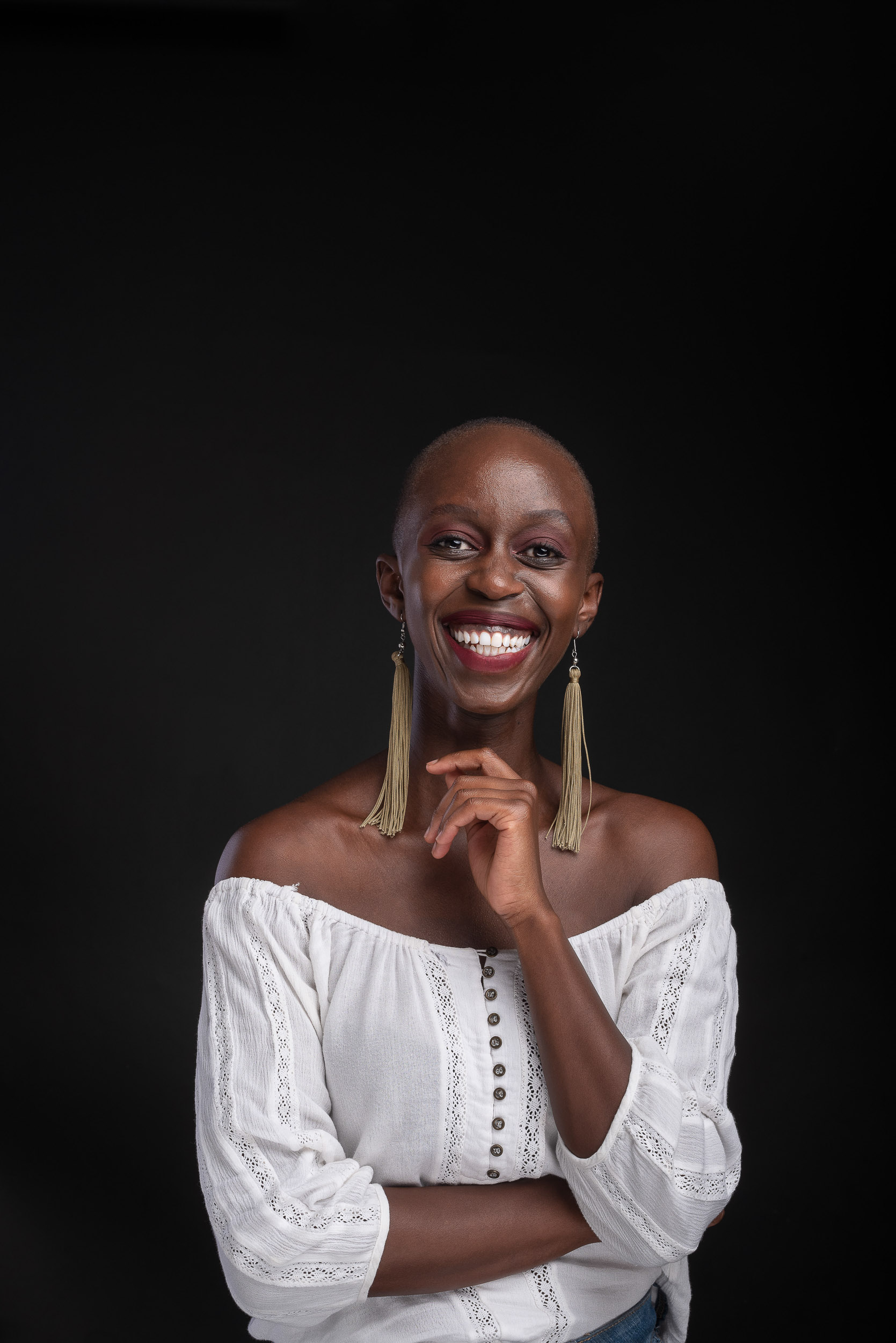 Studio portrait of a smiling woman in a white off-shoulder top with long beaded earrings on a black background