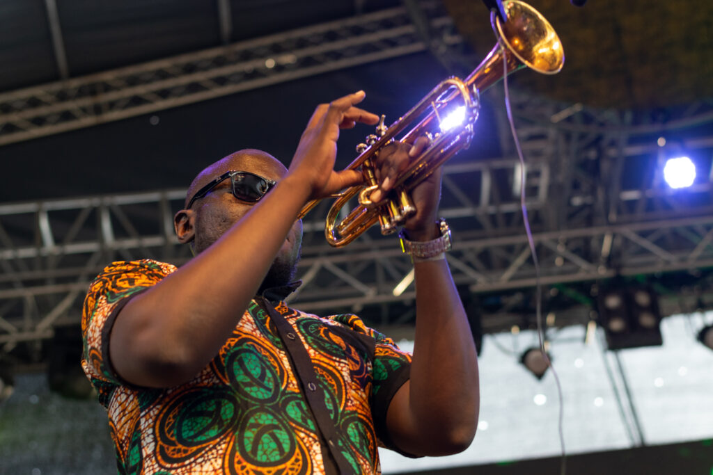 Trumpeter in a patterned shirt performing on stage under stage lights