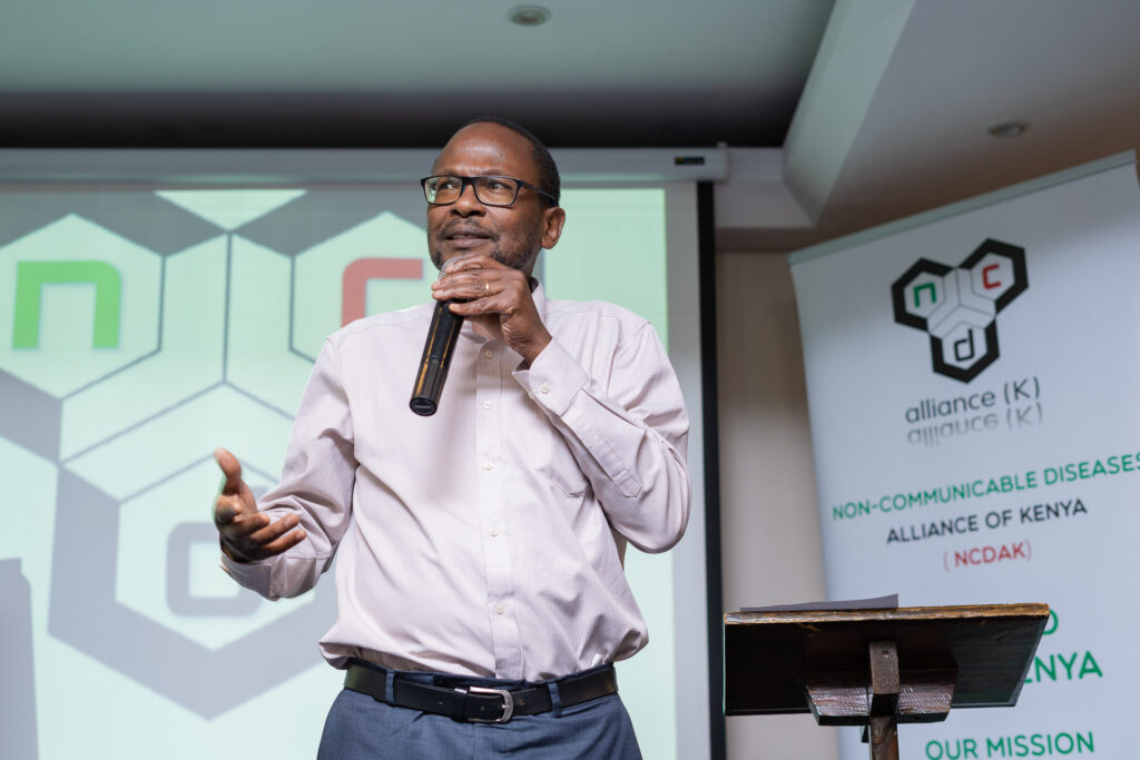 Speaker presenting with a microphone at a Non-Communicable Diseases Alliance of Kenya event