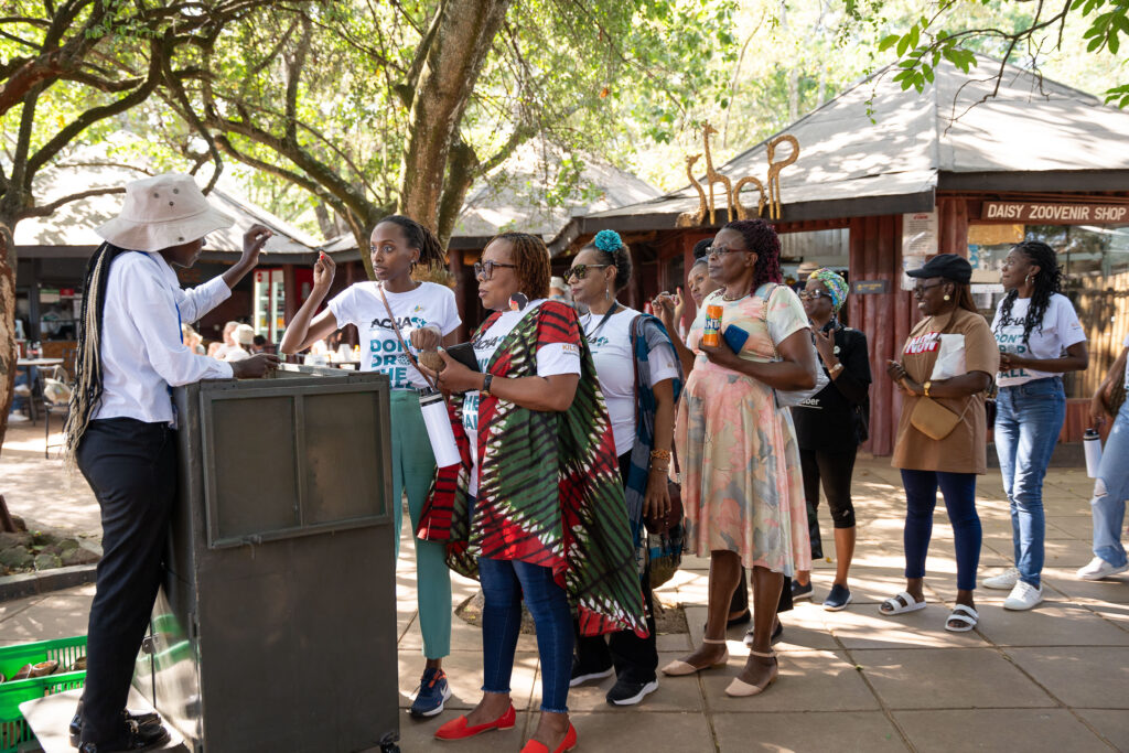 Outdoor gathering under trees with a speaker addressing attendees