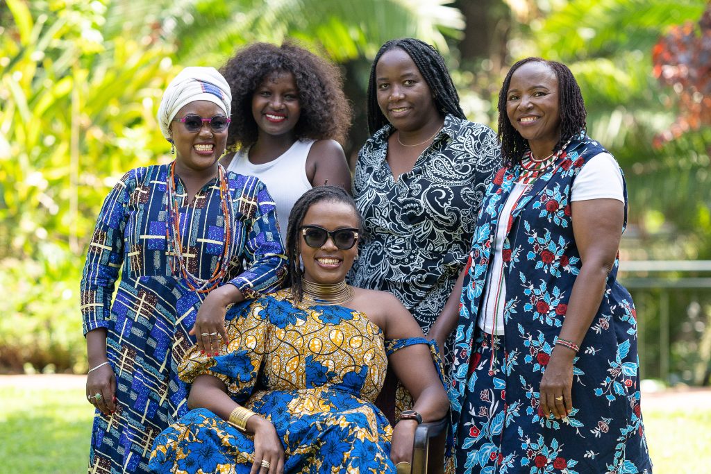 Five women in patterned dresses posing together outdoors